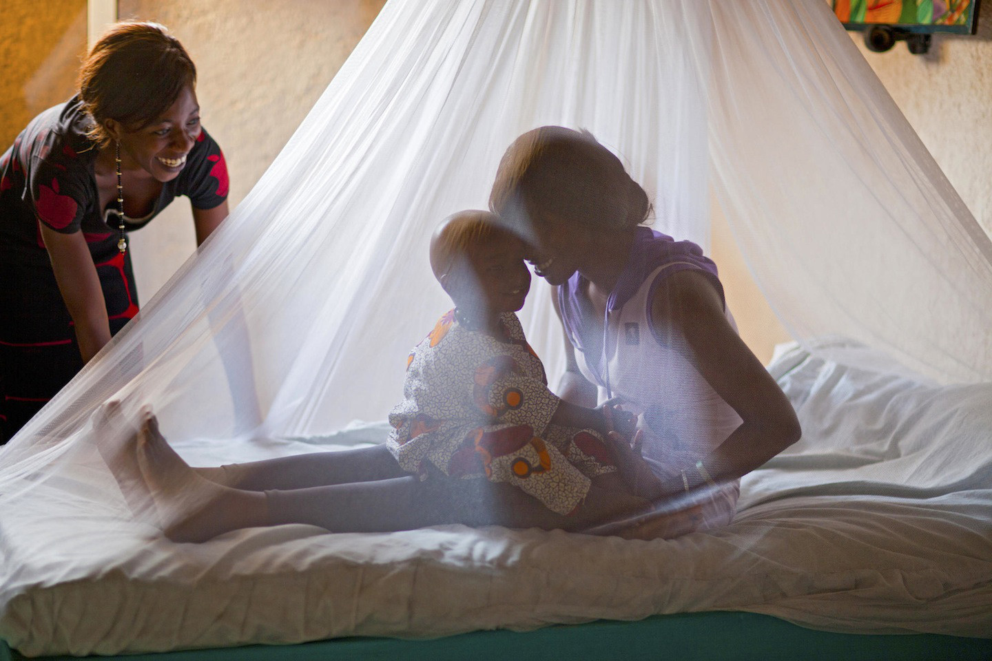 A mother and child wake up under a mosquito net.