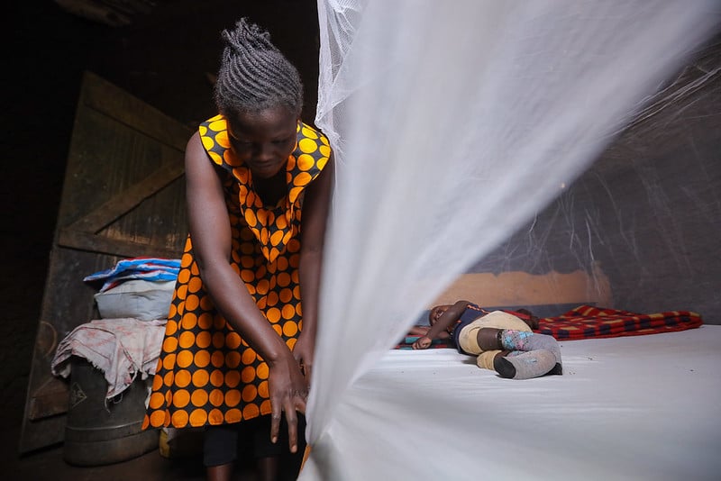 Mother in Mozambique is securing a bed net while a baby sleeps in bed